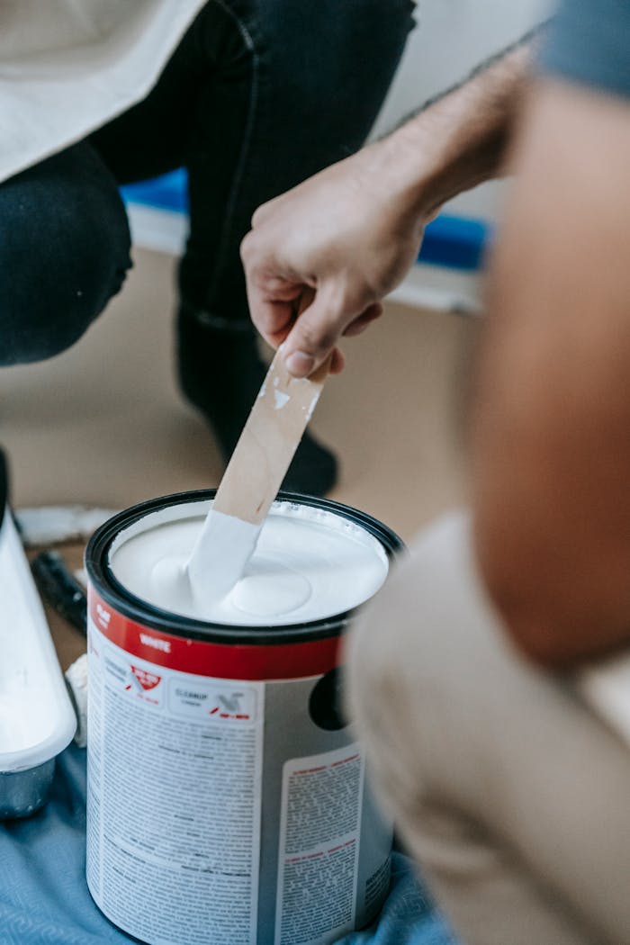Close-up of a person mixing white paint in a can, preparing for home renovation.